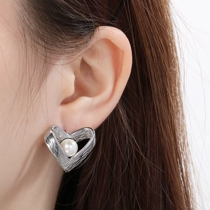 Close-up of vintage heart stud earring with brushed silver texture and pearl inlay