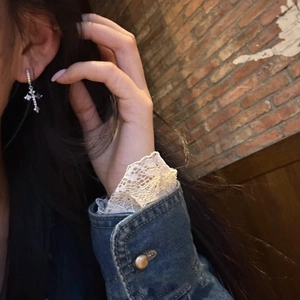 Close-up of a sparkling silver cross drop earring worn on ear with retro brick background