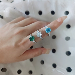 Macro shot of 2ct emerald cut moissanite rings in green, clear, and blue on finger