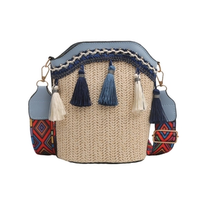 Detail of woven straw bucket bag with blue trim, bohemian tassel, and colorful wide strap