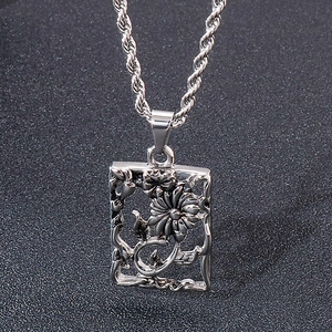 Macro shot of silver rectangle cutout floral pendant and twist chain necklace in steel