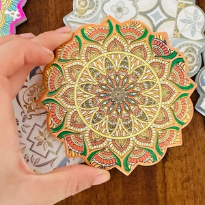 Detail of hand holding a mandala ceramic coaster with gold stamping and floral edges