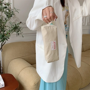 Handheld view of a beige pleated cosmetic bag and stationery pouch in a cozy room