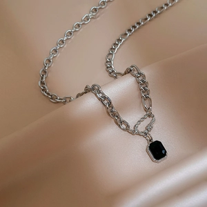 Close-up of geometric silver necklace with black rectangle pendant on silk fabric