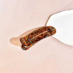Detailed view of an oval acetate hair clip with classic tortoiseshell and amber pattern