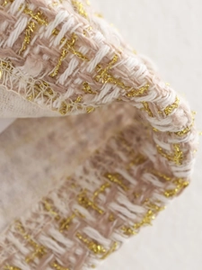 Macro detail of beige tweed fabric with woven gold metallic threads and rich texture