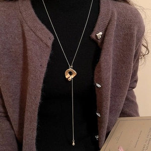 Detailansicht einer unregelmäßigen Goldhalskette mit glatter Flüssigmetall-Textur auf einem Pullover