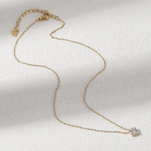 Close-up of gold-plated necklace with a zircon teardrop pendant and heart-shaped logo tag