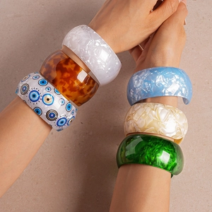 Close-up of vibrant acrylic open bangles in amber, marble, and eye patterns on wrist