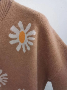 Close-up of knit sweater fabric with white daisy flower embroidery on brown background