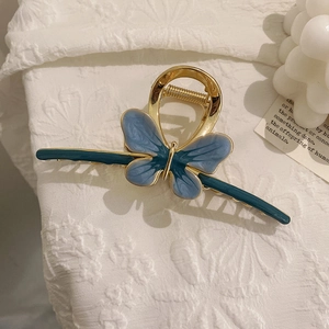 Macro shot of butterfly hair claw clip with blue enamel and gold tassel on white fabric