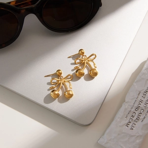 Detail of gold cherry bow earrings on a metal surface with warm natural lighting