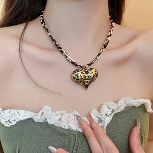 Detail shot of leopard print heart pendant on a gold necklace worn by a model