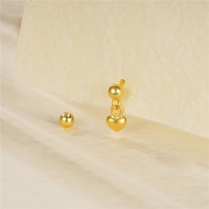 Close-up of a gold heart charm stud earring on a beige textured card and satin background