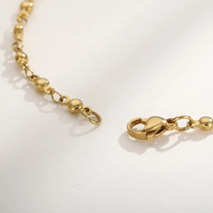 Macro detail of the golden bead chain bracelet showing lobster clasp and metallic finish