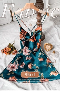Detailed view of dark green floral satin slip dress with cross-back straps on a wooden hanger