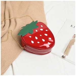 Detail of red strawberry-shaped crossbody bag with gold chain strap and glossy finish
