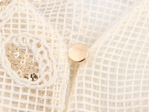 Close-up of elegant mesh lace fabric with golden sequin embroidery and a gold metal button