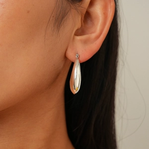Close-up of polished silver teardrop hoop earring worn to show scale and metallic shine