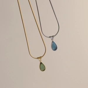Detail of drop-shaped pendants in green and blue on elegant gold and silver snake chains