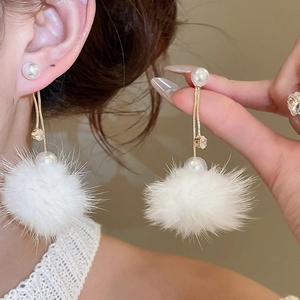 Detail of long drop earrings featuring fluffy white pom poms, gold chains and pearls