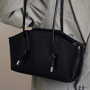 Minimalist black trapezoid shoulder bag with unique knotted straps and metallic detail