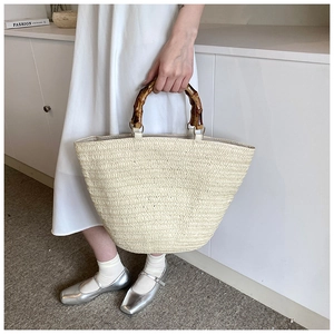 Detail of the woven tote bag featuring natural bamboo handles and creamy white texture