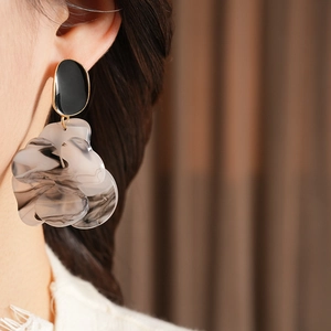 Close-up of model wearing large flower earrings with black studs and smoky grey petals