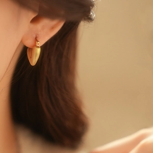 Close-up of golden matte heart-shaped earrings on model with soft lighting