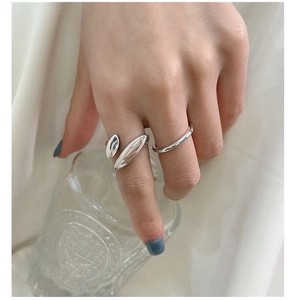 Close-up of minimalist silver rings worn on hand against a clean fabric background