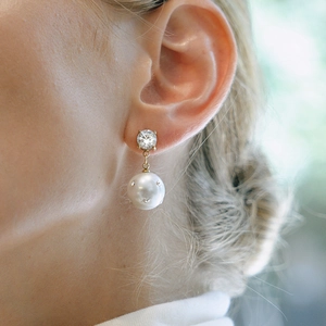Elegante Ohrringe aus Titanstahl in Gold mit großem Diamanten und Perle an einer Frau