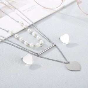 Three-layer silver heart necklace set with pearls and matching studs on a textured base