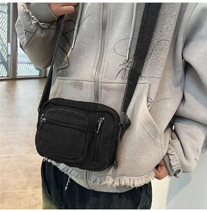 Detail view of black washed denim crossbody bag with silver zippers and adjustable strap