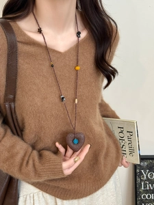 Detailed view of heart pendant sweater chain with blue bead on a model wearing V-neck knitwear