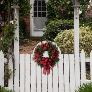 Christmas wreath with red berries and black-red plaid bow on white wooden fence