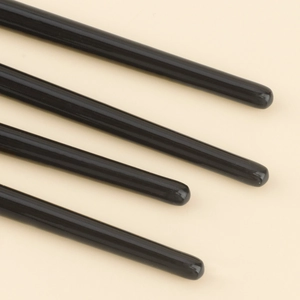 Detailed macro view of four professional black glossy makeup brush handles on beige background