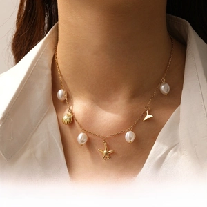 Detail of gold-plated necklace with sea shell, starfish, fish tail charms and white pearls
