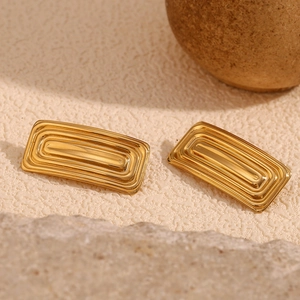 Close-up of gold rectangular earrings with geometric stepped texture on sand background