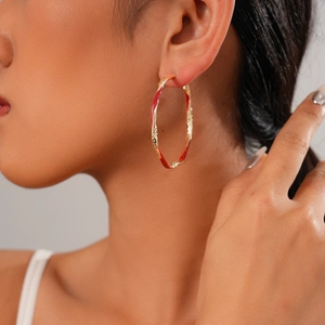 Close-up of a large gold twisted earring with vibrant red enamel on female model