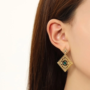 Macro detail of vintage hollow gold earrings with green square gemstones on model