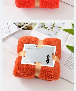 Detail of vibrant orange coral fleece face towel folded with a silk ribbon in a basket