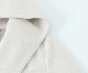 Detailed close-up of soft oatmeal wool texture and stitching on the hooded coat