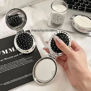 Portable folding hairbrush with mirror in silver metallic finish on a desk
