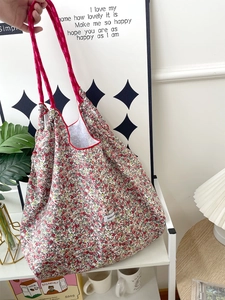 Detailed close-up of floral canvas tote bag with red woven handle and white logo label