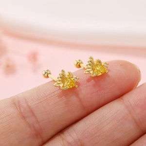 Macro shot of gold-plated butterfly wing cartilage studs with yellow gemstones on fingertip