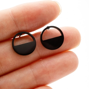 Macro shot of black geometric circular stainless steel stud earrings held between fingers