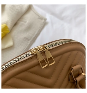 Detail of gold double-zipper hardware and V-quilted faux leather on a beige shell handbag