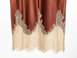 Detail of burgundy satin skirt hem featuring delicate cream eyelash lace trim