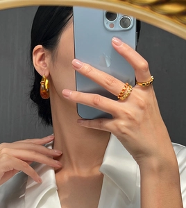 Mirror selfie showing gold U-shaped earrings with amber resin and gemstone rings