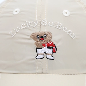 Macro-opname van beerborduurwerk en Lucky So Bear-tekst op de beige baseballpet van dichtbij